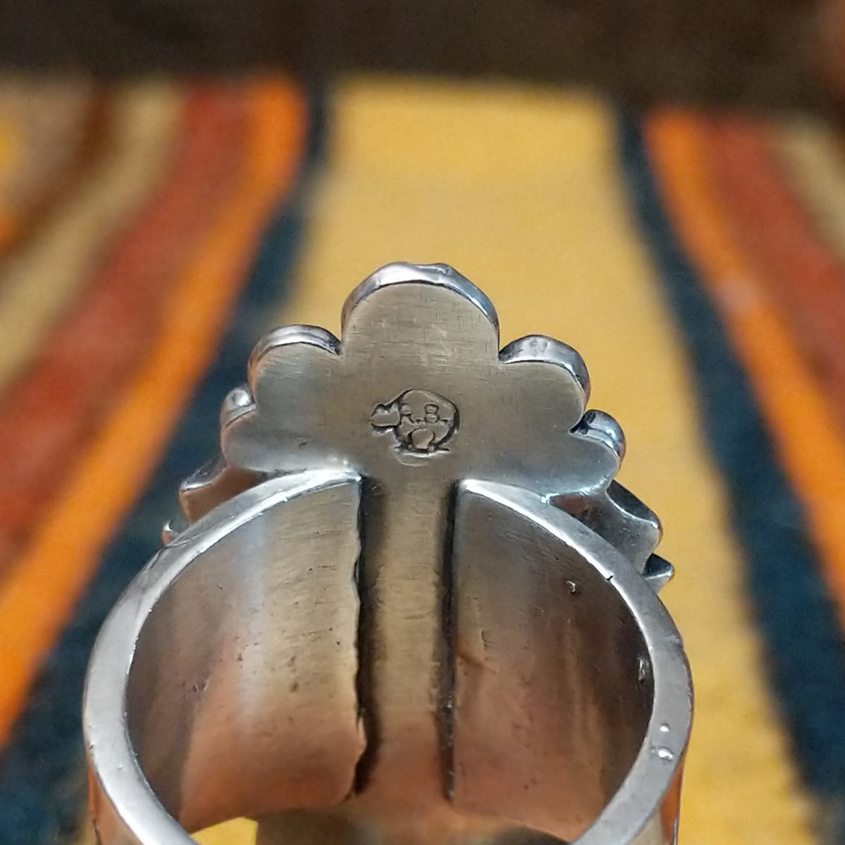 This elegant Navajo Ornate Sonoran Gold Turquoise Ring features a large oval blue turquoise stone surrounded by a silver rope border, polished silver beads, and decorative stamped silver blossoms; artisan stamp.