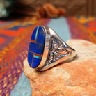 Navajo Oval Lapis Inlay Ring by T.L. featuring geometric blue lapis inlay with turquoise and red accents, Sterling Silver channels, and detailed stamped silverwork; side view.