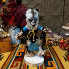 Navajo Protection Dancer Kachina doll with gray fur headdress, black painted facial markings, blue sleeves, feather accents, and raised foot.