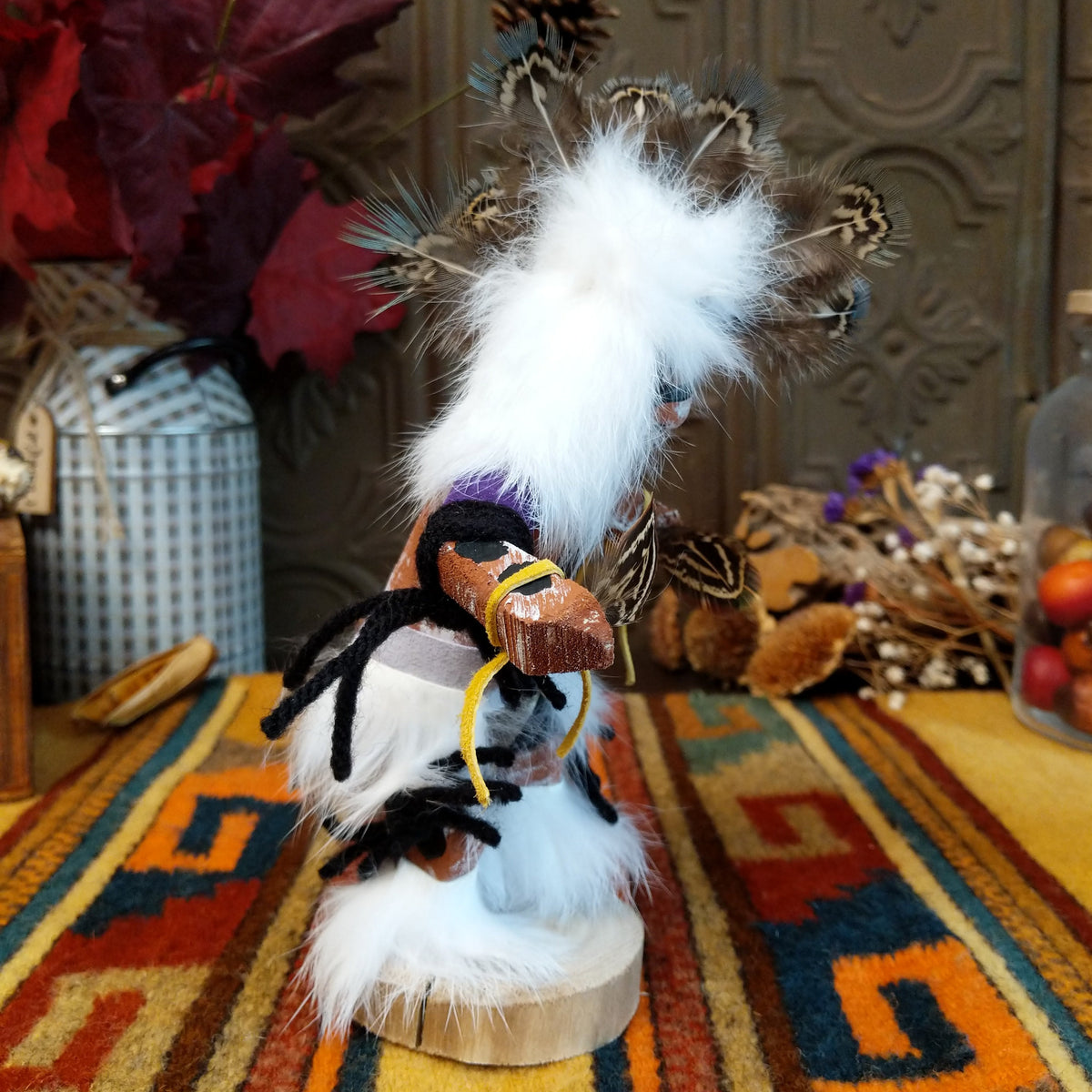 This distinctive Navajo Protection Dancer Kachina by Debbie James features a hand-painted wooden figure with a white feather headdress, natural feathers, leather ties, fur accents, colorful fabric details, and a wooden display base; side view.