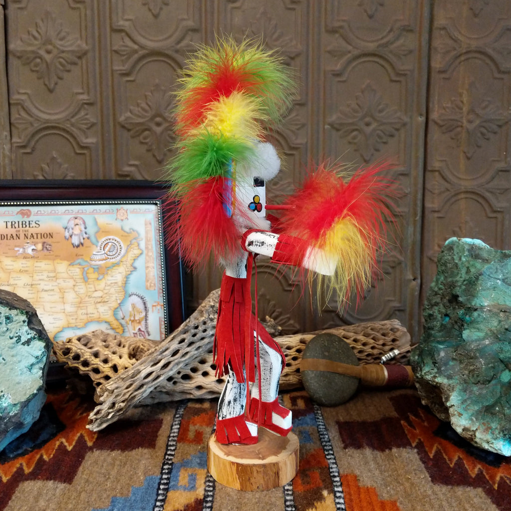 Wood carved into the rainbow kachina, vibrant multicolored paints and feathers and red suede clothing.