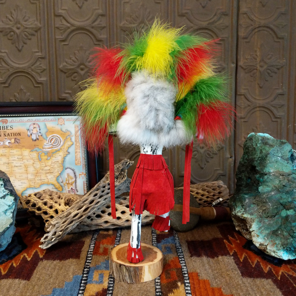 Wood carved into the rainbow kachina, vibrant multicolored paints and feathers and red suede clothing.