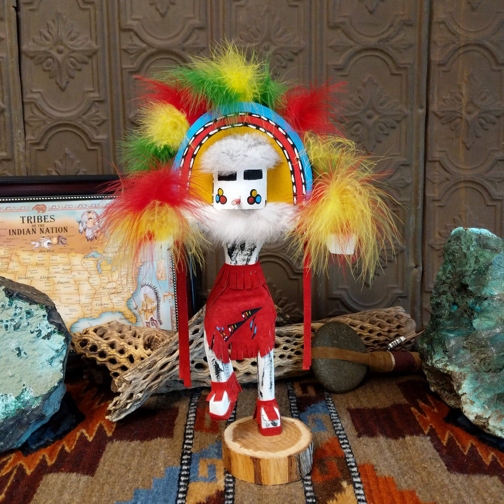 Wood carved into the rainbow kachina, vibrant multicolored paints and feathers and red suede clothing.