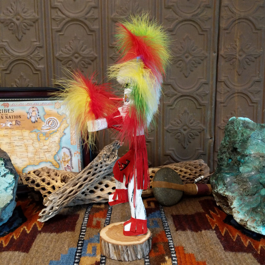 Wood carved into the rainbow kachina, vibrant multicolored paints and feathers and red suede clothing.