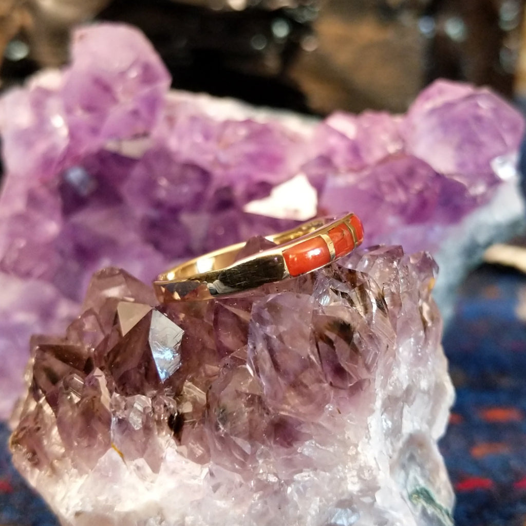 Navajo-style ring showing red coral inlay segments in a polished gold setting.
