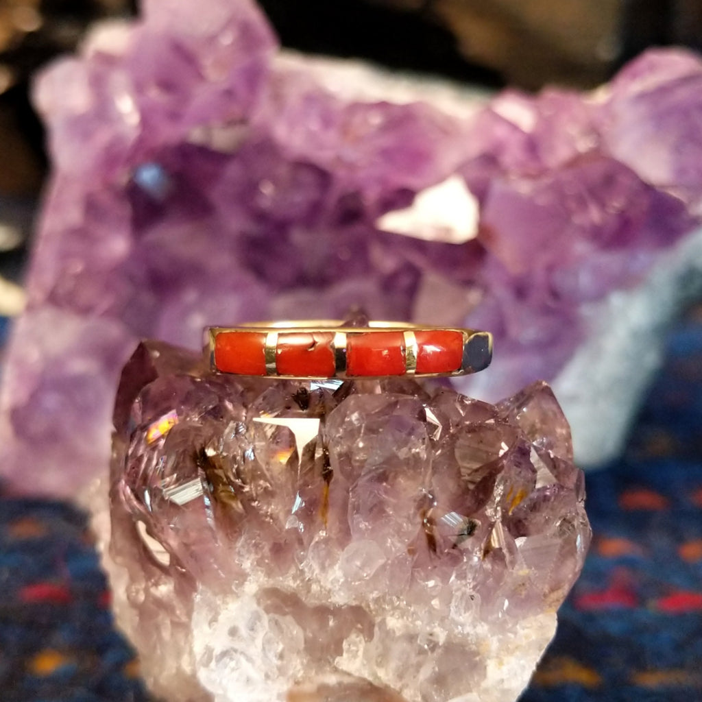 Navajo-style ring showing red coral inlay segments in a polished gold setting.