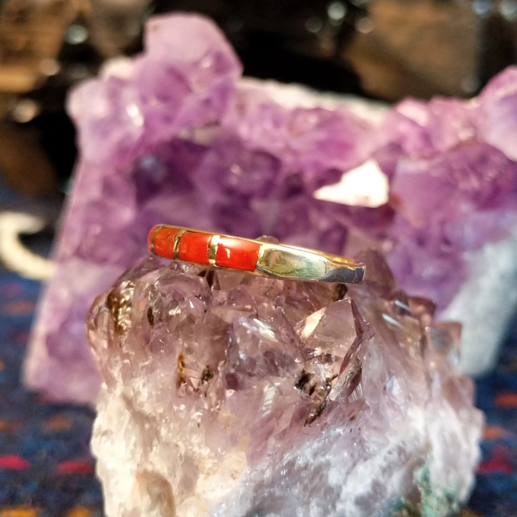 Navajo-style ring showing red coral inlay segments in a polished gold setting.