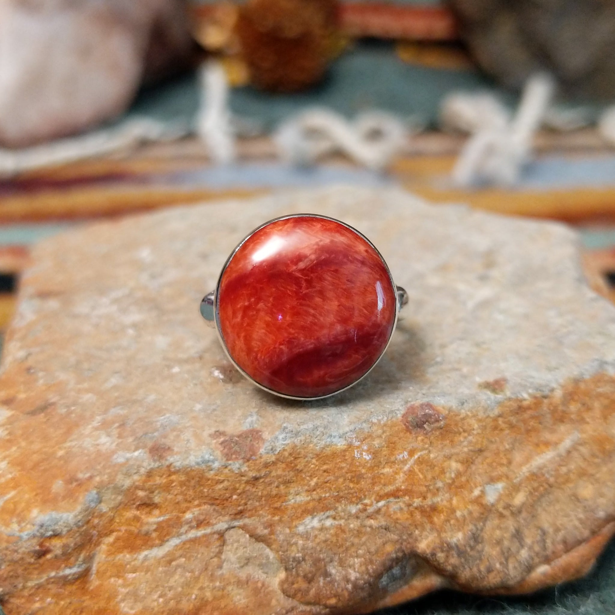 Navajo sterling silver ring by N.A. featuring a round red spiny oyster shell cabochon with natural color variations in a smooth silver bezel.