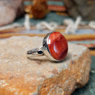 Navajo sterling silver ring by N.A. featuring a round red spiny oyster shell cabochon with natural color variations in a smooth silver bezel; side view.