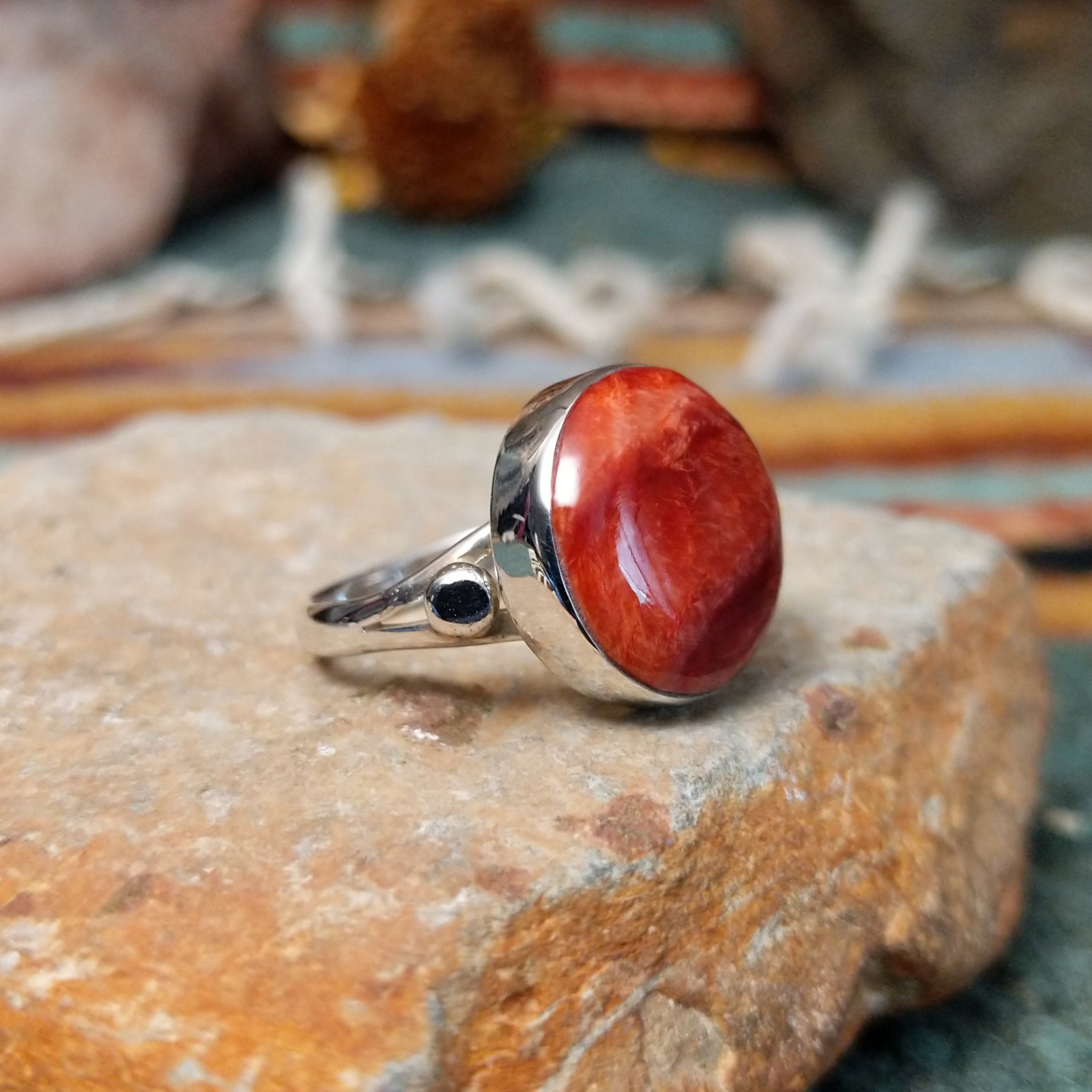 Navajo sterling silver ring by N.A. featuring a round red spiny oyster shell cabochon with natural color variations in a smooth silver bezel; side view.