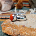 Navajo sterling silver ring by W.B.V. featuring a smooth oval red coral cabochon set in a polished silver bezel and band; side view.
