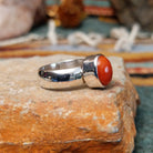 Navajo sterling silver ring by W.B.V. featuring a smooth oval red coral cabochon set in a polished silver bezel and band; side view.