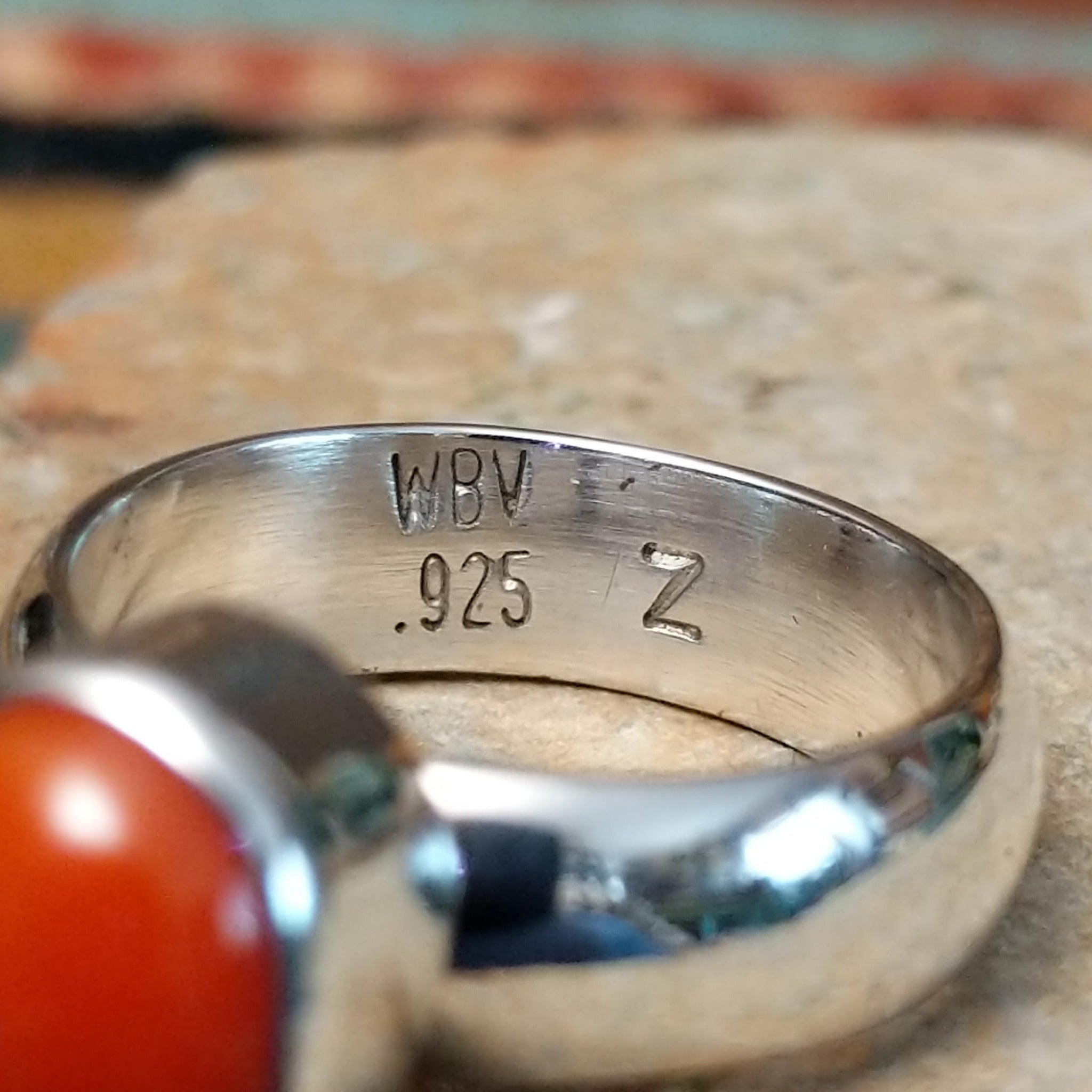 Navajo sterling silver ring by W.B.V. featuring a smooth oval red coral cabochon set in a polished silver bezel and band; artisan and .925 (Sterling Silver) stamp.