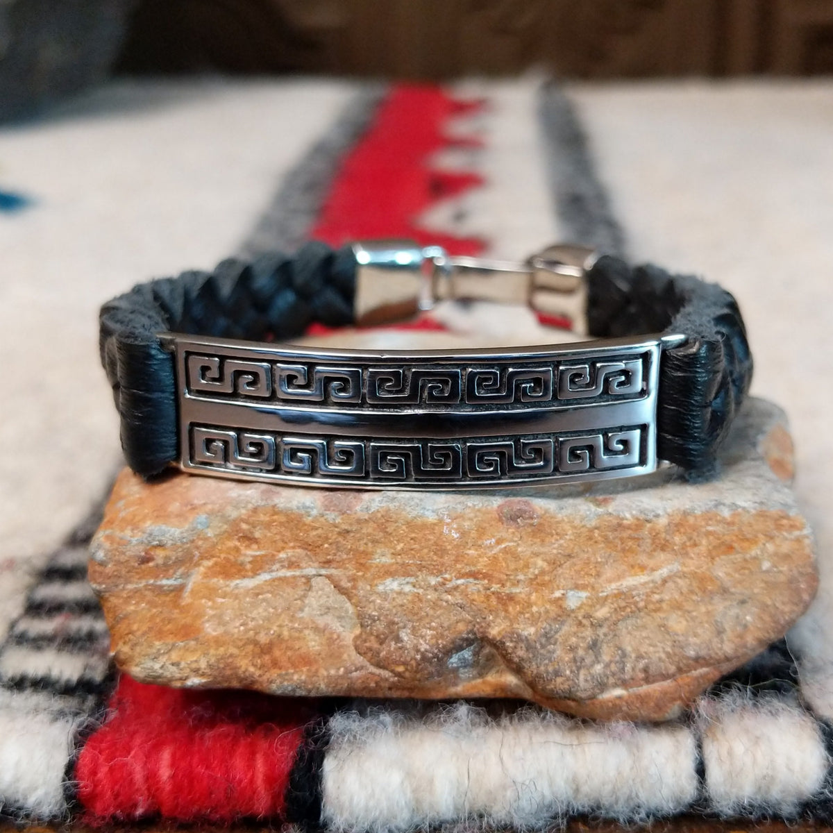 Navajo bracelet featuring braided black leather and a rectangular silver centerpiece with two rows of repeating geometric scroll patterns and darkened recessed details.
