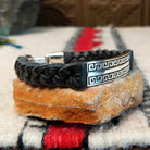 Navajo bracelet featuring braided black leather and a rectangular silver centerpiece with two rows of repeating geometric scroll patterns and darkened recessed details; side view.