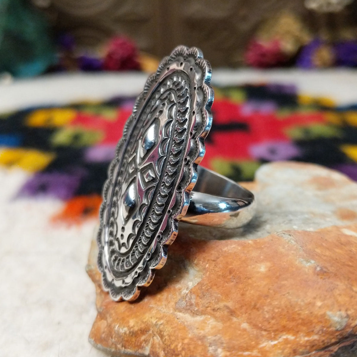 Navajo Silver Concho Ring with an elongated oval shape, raised diamond motifs, detailed stamped silverwork, oxidized accents, and a scalloped border; side view.