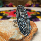 Navajo Silver Concho Ring with an elongated oval shape, raised diamond motifs, detailed stamped silverwork, oxidized accents, and a scalloped border; side view.