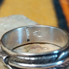 Close-up of the inside of a silver feather-patterned ring showing a vertical sterling stamp and a stamped hallmark.
