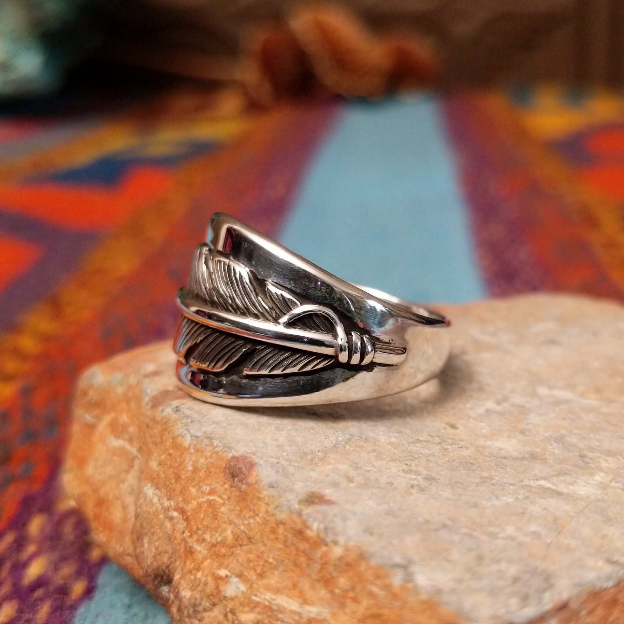 Navajo Silver Feather Ring by L.P. featuring a detailed engraved feather with a raised curved quill across a wide, polished silver band; side view.