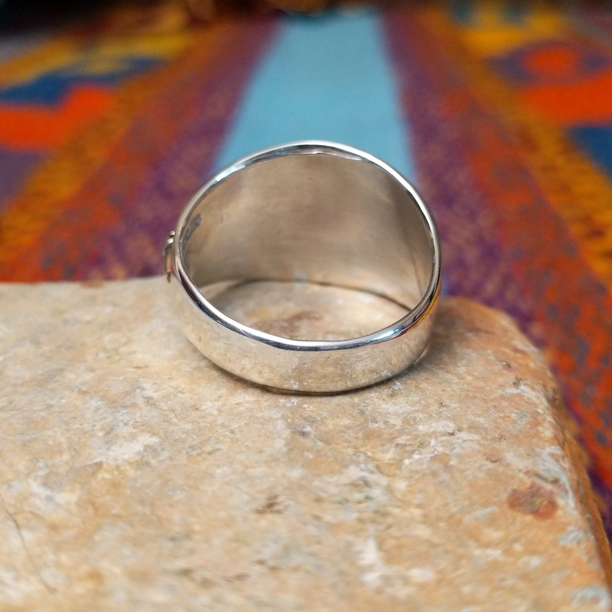 Navajo Silver Feather Ring by L.P. featuring a detailed engraved feather with a raised curved quill across a wide, polished silver band; underside view.