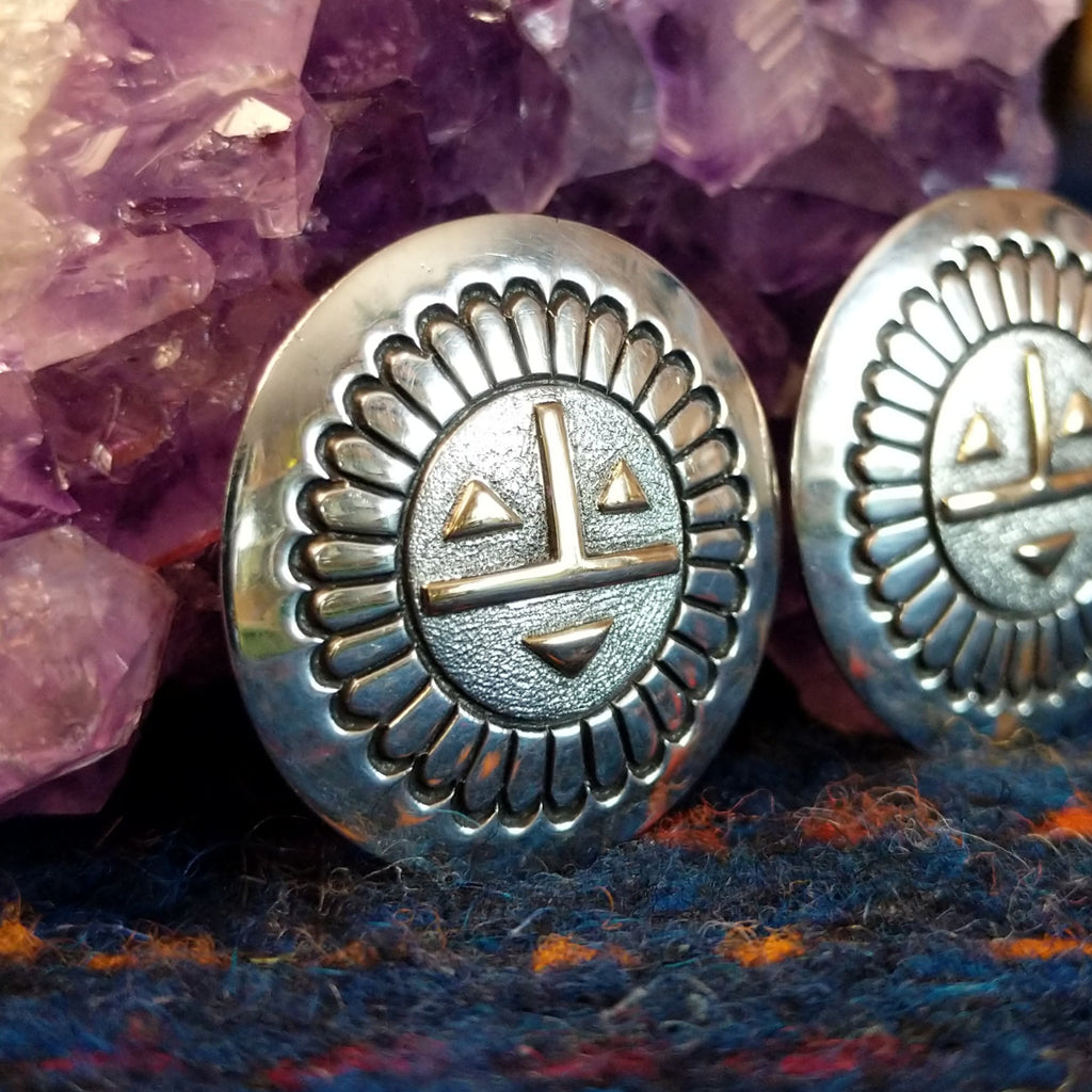 The earrings showing detailed stamping, geometric gold facial accents, and polished silver finish.