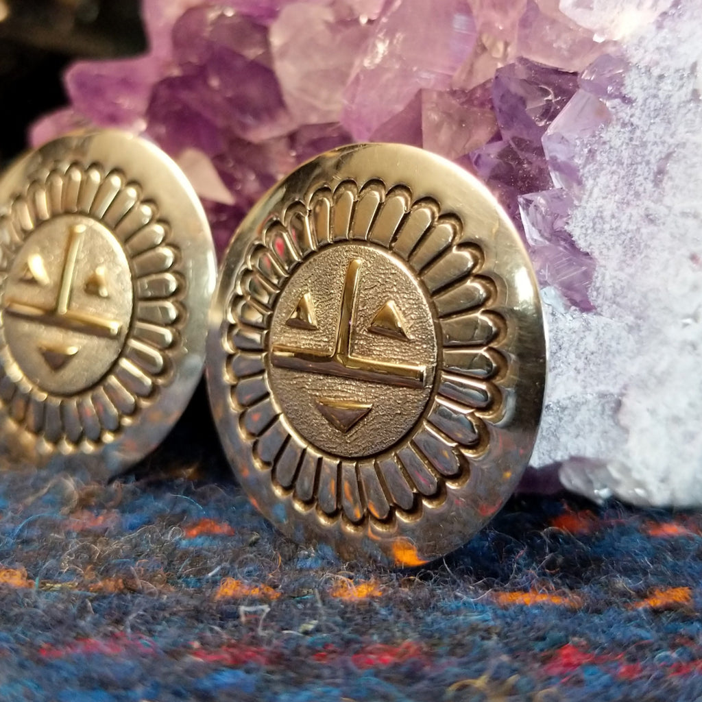 The earrings showing detailed stamping, geometric gold facial accents, and polished silver finish.