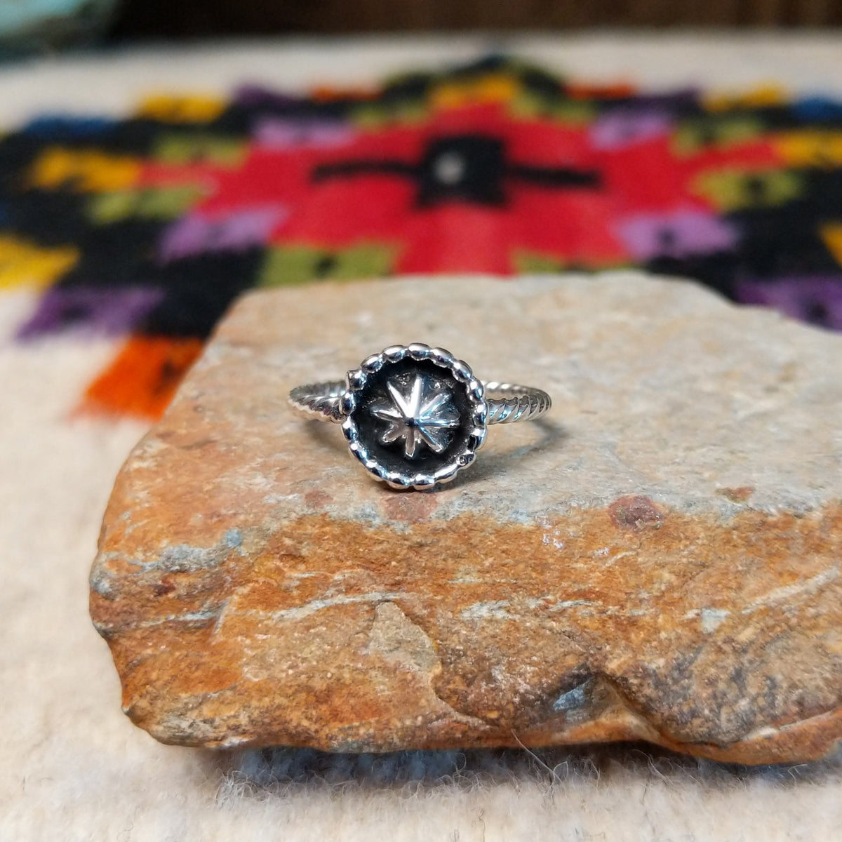 This Navajo Silver Star Ring features a round sterling silver face with a polished starburst design, dark oxidized background, beaded border, and textured silver band.