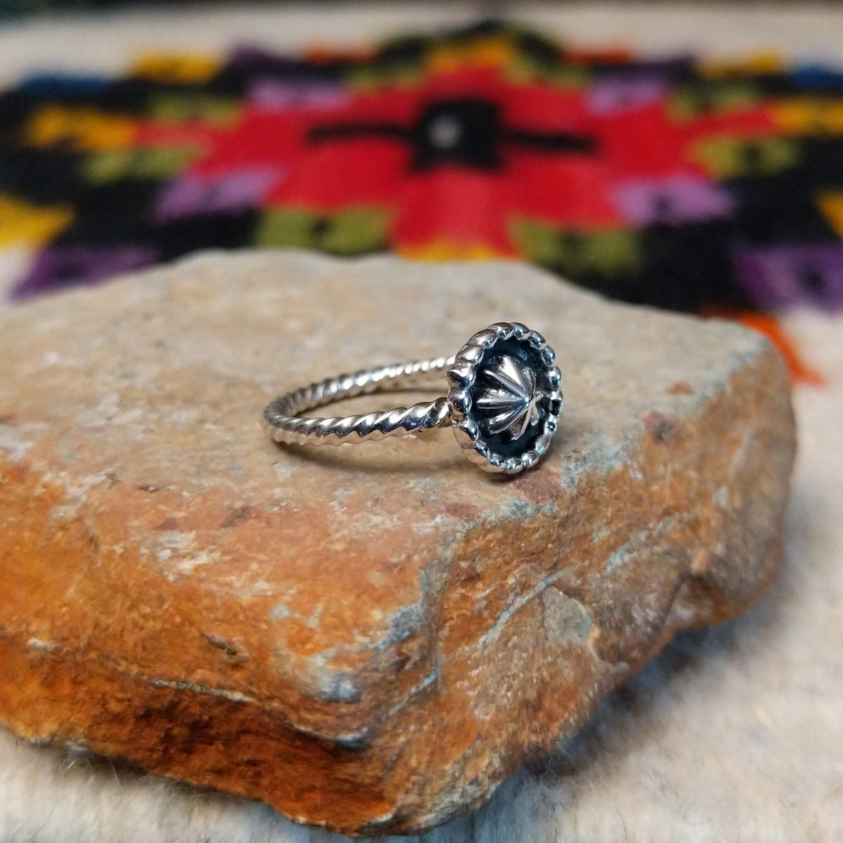 This Navajo Silver Star Ring features a round sterling silver face with a polished starburst design, dark oxidized background, beaded border, and textured silver band; side view.