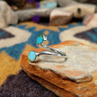 Handcrafted Navajo sterling silver bypass ring featuring two oval Sonoran Gold turquoise cabochons in smooth bezel settings, with vibrant blue and green natural turquoise on a polished open-band design; side view.