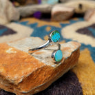 Handcrafted Navajo sterling silver bypass ring featuring two oval Sonoran Gold turquoise cabochons in smooth bezel settings, with vibrant blue and green natural turquoise on a polished open-band design; side view.