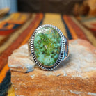 Navajo Sonoran Gold Turquoise Ring by S.N. featuring a large oval green and turquoise stone with natural matrix patterns, a twisted silver rope border, and a wide silver band with stamped sunburst detailing.