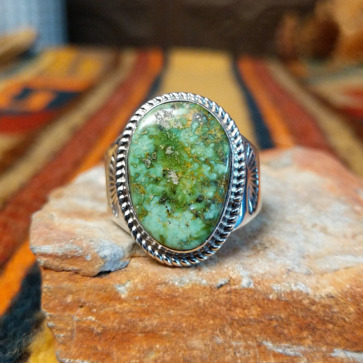 Navajo Sonoran Gold Turquoise Ring by S.N. featuring a large oval green and turquoise stone with natural matrix patterns, a twisted silver rope border, and a wide silver band with stamped sunburst detailing.
