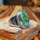 Navajo Sonoran Gold Turquoise Ring by S.N. featuring a large oval green and turquoise stone with natural matrix patterns, a twisted silver rope border, and a wide silver band with stamped sunburst detailing; side view.