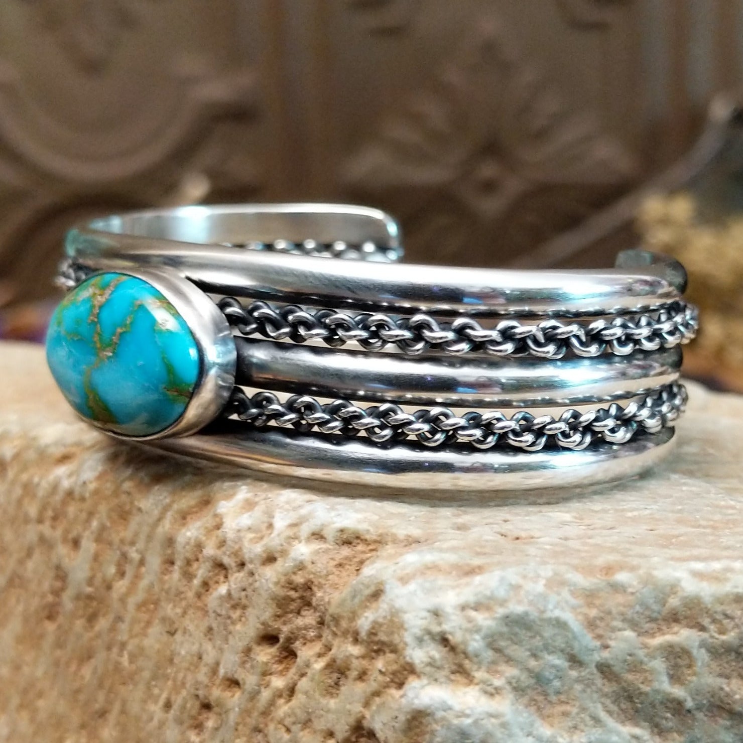 Sterling silver cuff with turquoise set in an oval bezel and chain-like designs on the band.