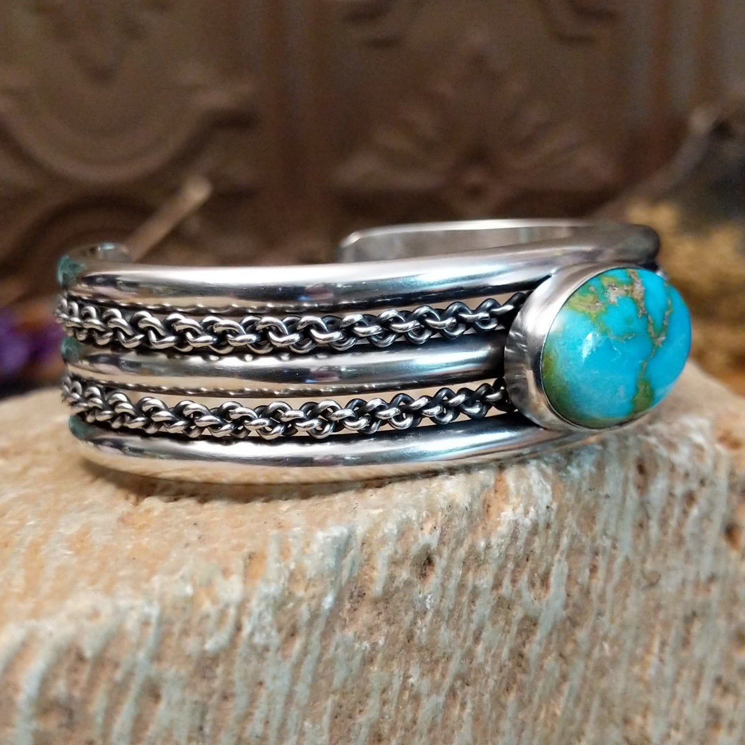 Sterling silver cuff with turquoise set in an oval bezel and chain-like designs on the band.