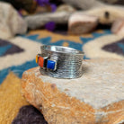 Navajo sterling silver textured band ring with three square gemstones in yellow, red, and blue; side view.