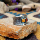 Navajo sterling silver textured band ring with three square gemstones in yellow, red, and blue; side view.