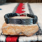 Navajo bracelet featuring braided black leather and a rectangular silver centerpiece decorated with repeating geometric stepped designs and dark oxidized accents.