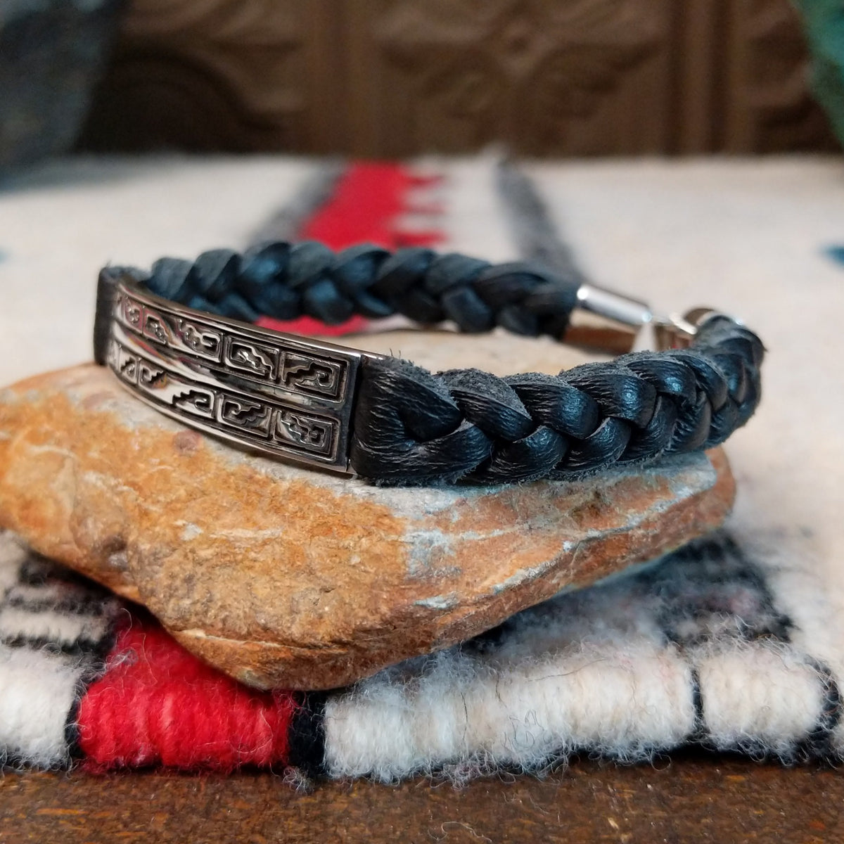Navajo bracelet featuring braided black leather and a rectangular silver centerpiece decorated with repeating geometric stepped designs and dark oxidized accents; side view.