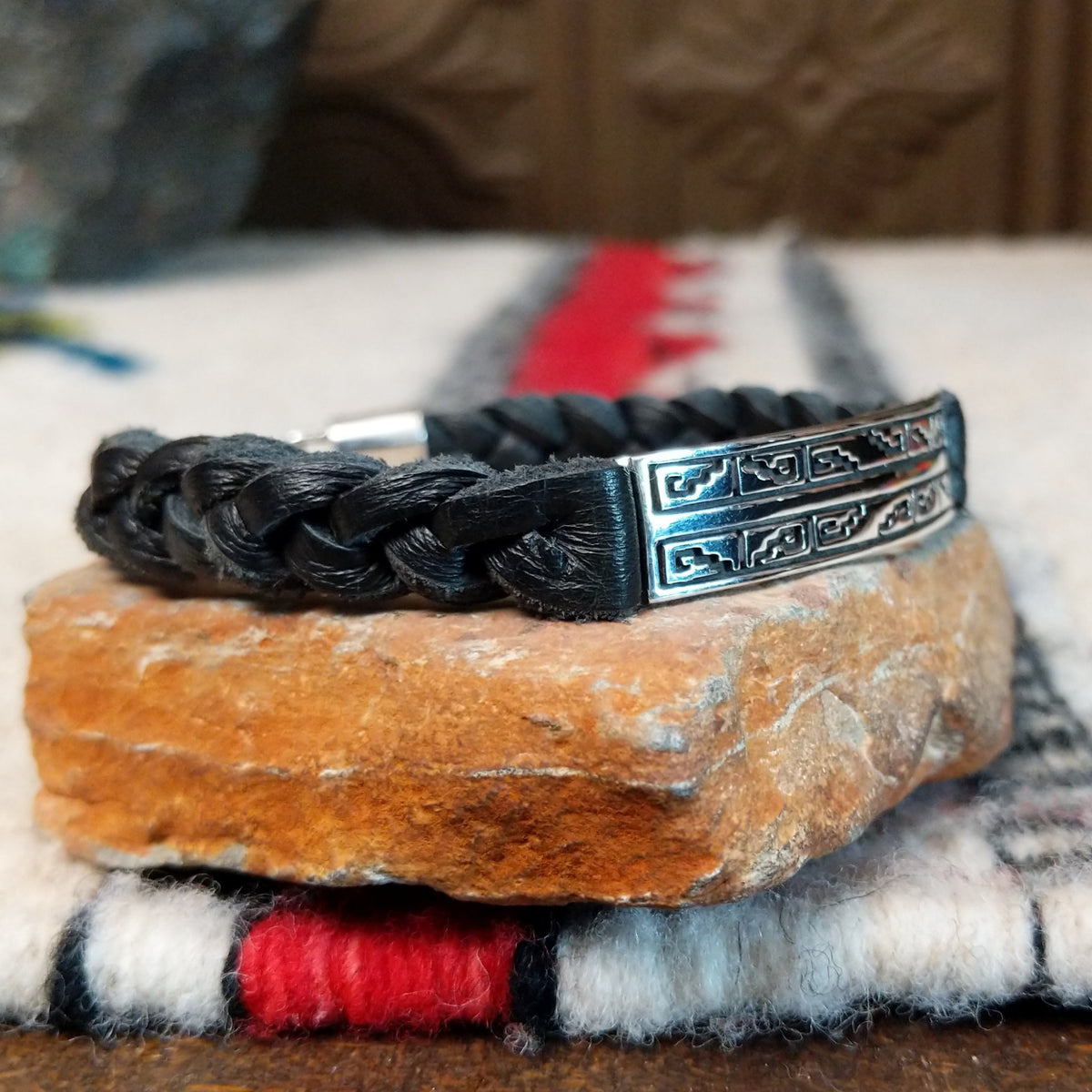 Navajo bracelet featuring braided black leather and a rectangular silver centerpiece decorated with repeating geometric stepped designs and dark oxidized accents; side view.