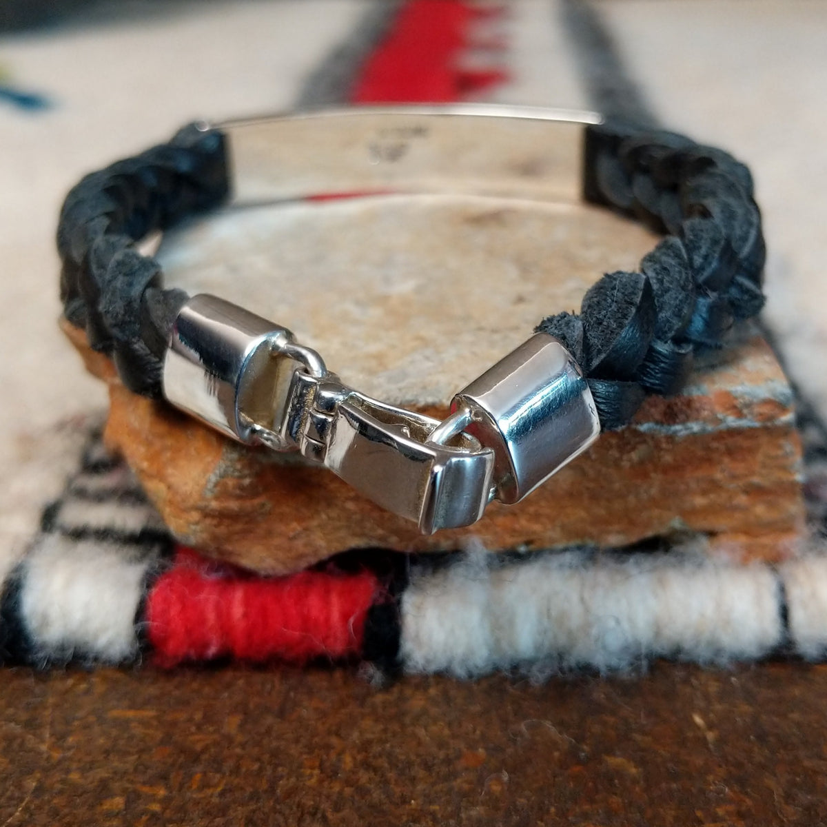 Navajo bracelet featuring braided black leather and a rectangular silver centerpiece decorated with repeating geometric stepped designs and dark oxidized accents; clasp view.
