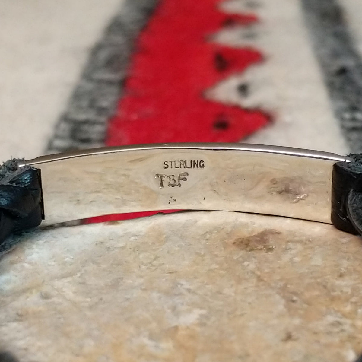 Navajo bracelet featuring braided black leather and a rectangular silver centerpiece decorated with repeating geometric stepped designs and dark oxidized accents; artisan and Sterling Silver stamp.