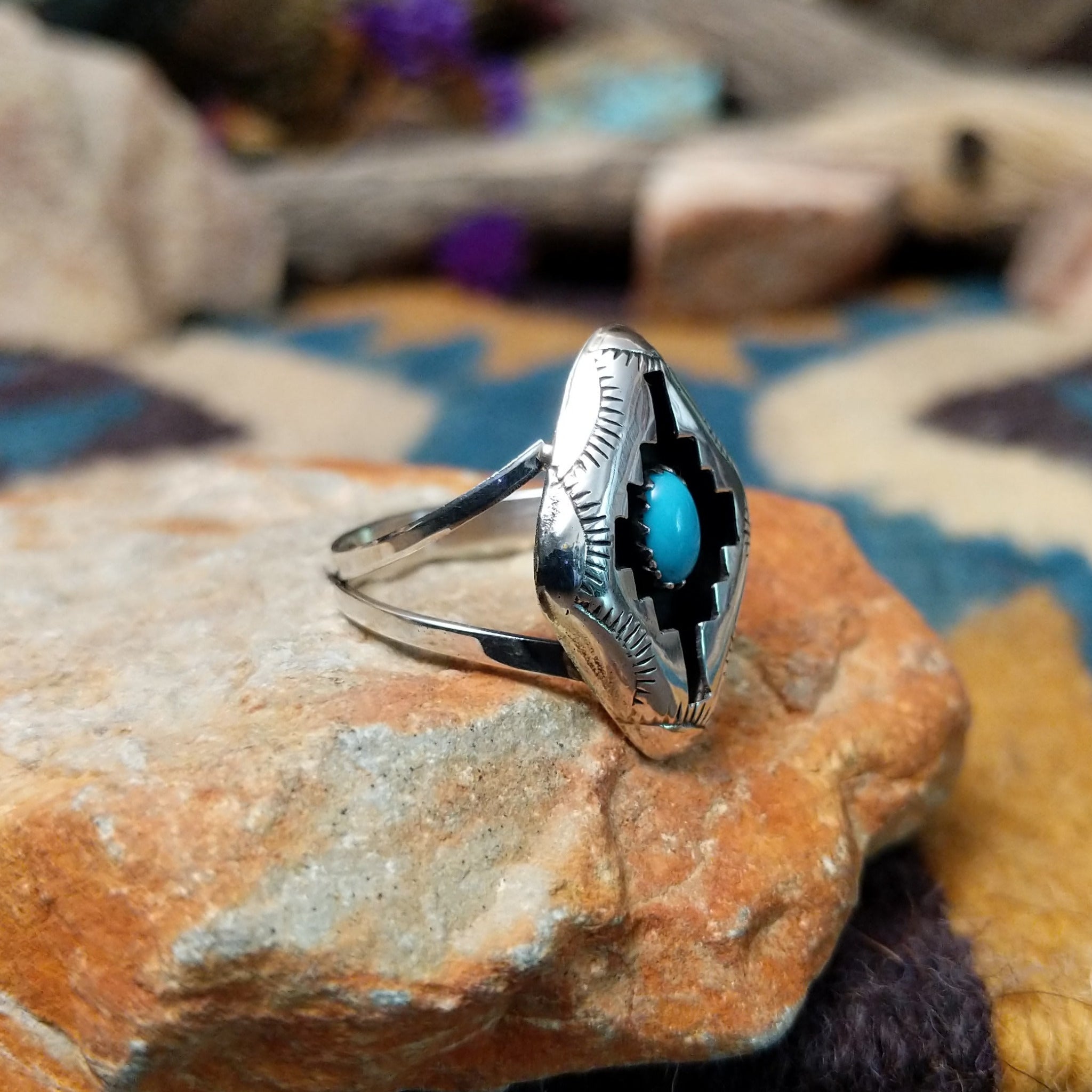 Handcrafted Navajo sterling silver shadowbox ring by P. featuring an oval turquoise cabochon set within a stepped geometric shadowbox design with hand-stamped details and an oxidized finish; side view.