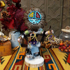 Navajo Sunface Kachina doll with turquoise-colored face, feather headdress, outstretched arms, and blue fabric clothing.