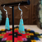 Navajo triangular turquoise slab earrings featuring bright blue stones with subtle tan and brown matrix, suspended from silver hooks; side view.