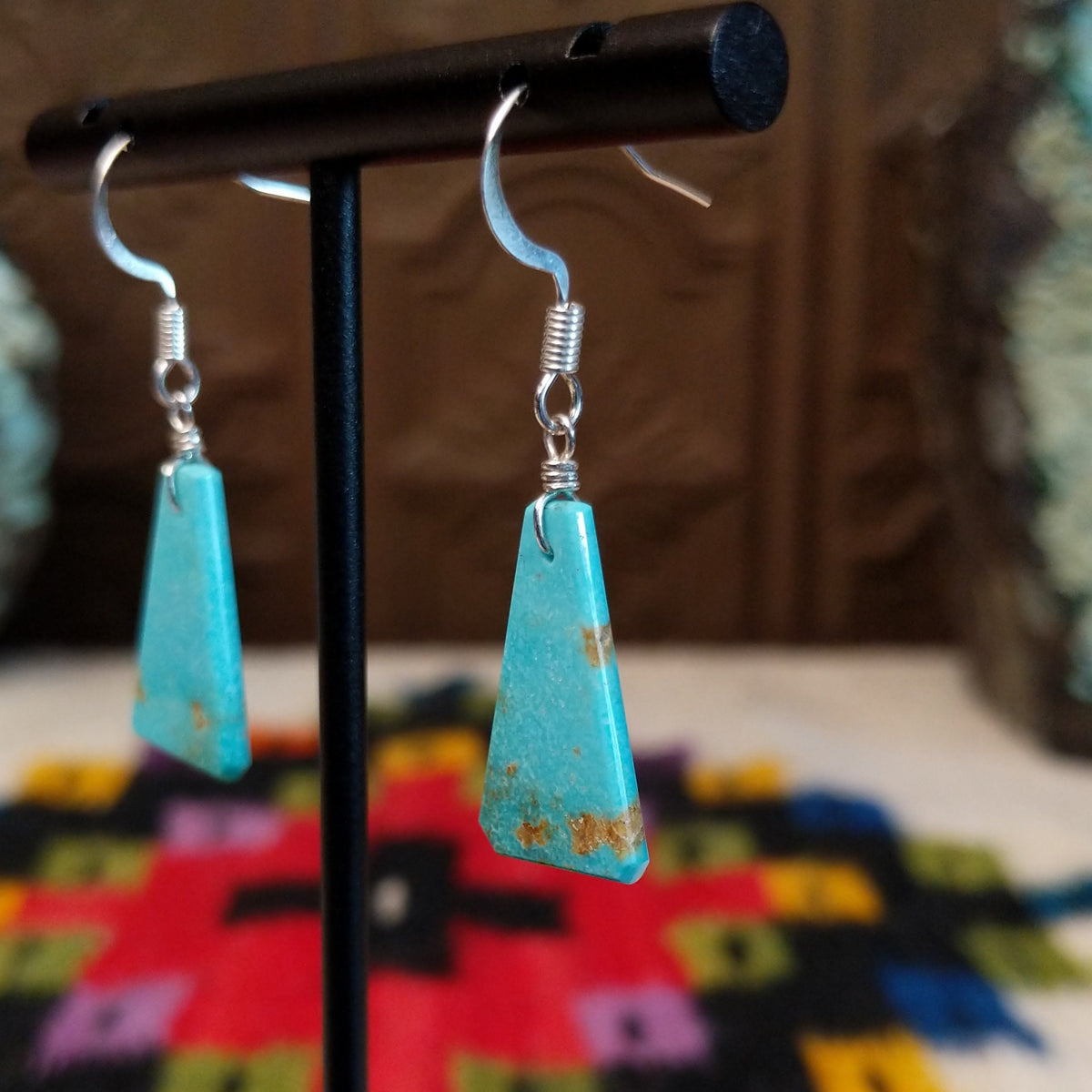 Navajo triangular turquoise slab earrings featuring bright blue stones with subtle tan and brown matrix, suspended from silver hooks; side view.