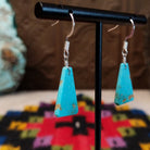 Navajo triangular turquoise slab earrings featuring bright blue stones with subtle tan and brown matrix, suspended from silver hooks; side view.