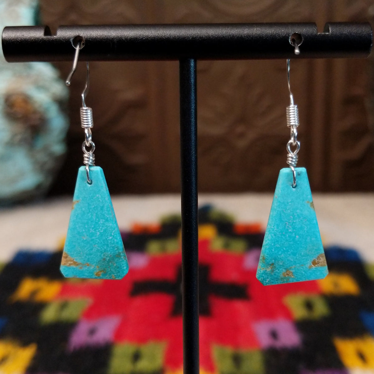 Navajo triangular turquoise slab earrings featuring bright blue stones with subtle tan and brown matrix, suspended from silver hooks; backside view.