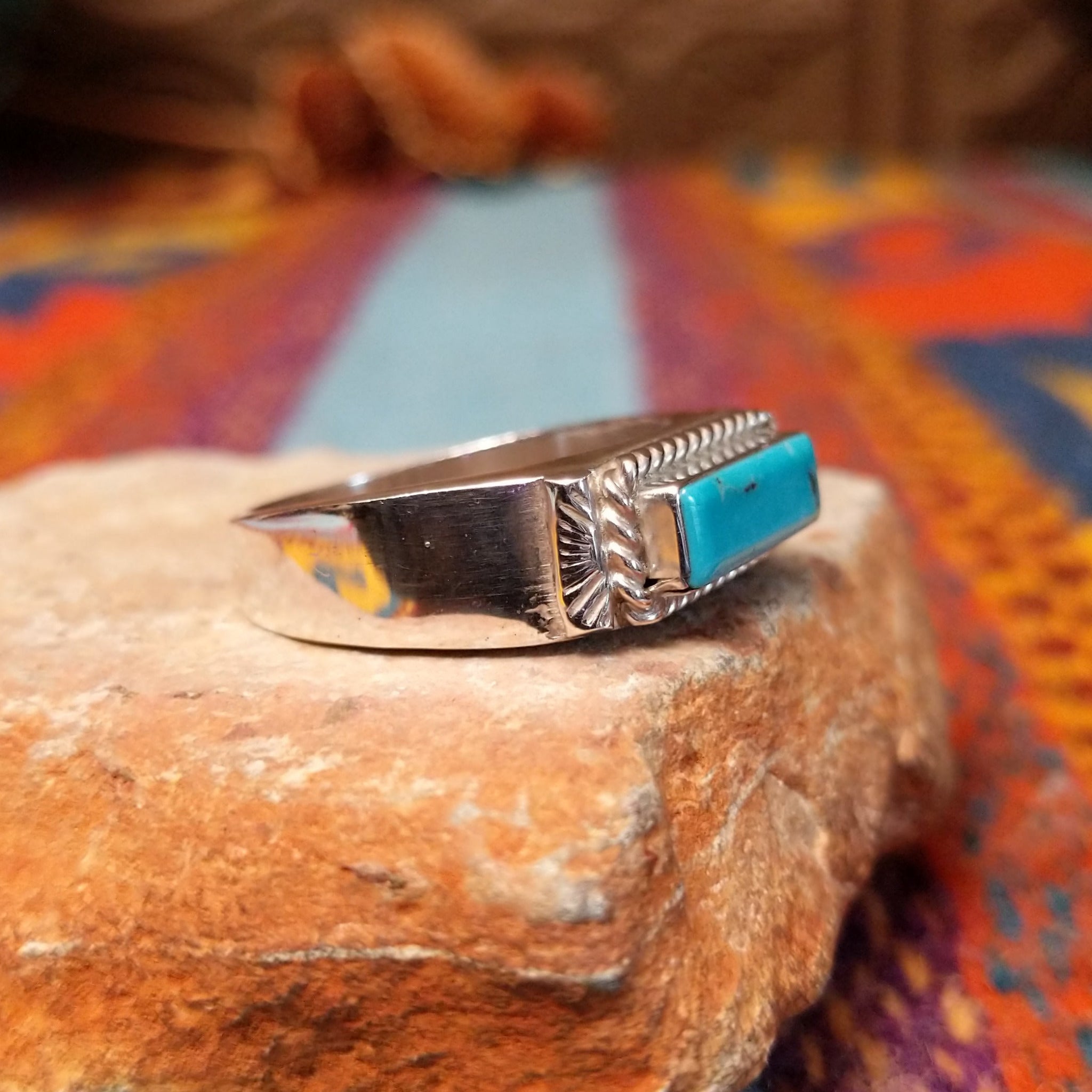 Navajo Turquoise Bar Ring by A.Q.J. featuring a rectangular bright blue turquoise stone with subtle matrix, framed by twisted-rope silverwork and decorative stamped details; side view.