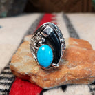 Navajo silver ring featuring a dark bear claw, oval turquoise stone, and detailed feather, scroll, and bead-style silverwork in an elongated statement design.